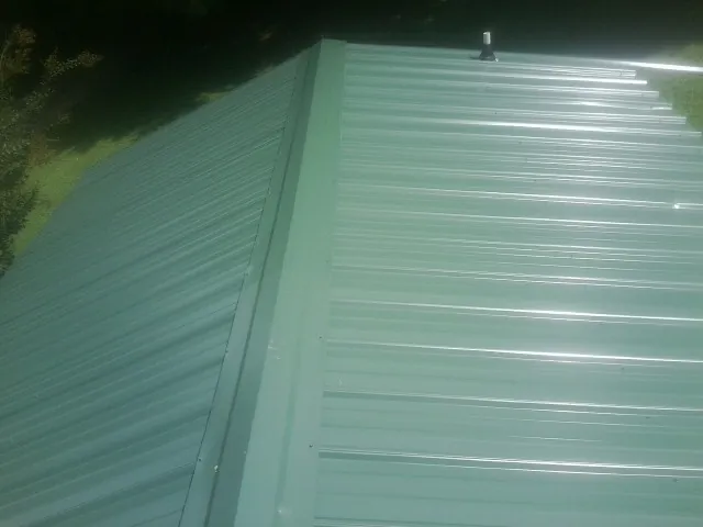 New green metal panels meeting at the ridge of a roof — Flat Roof Repair work by our crew in Fort Lee